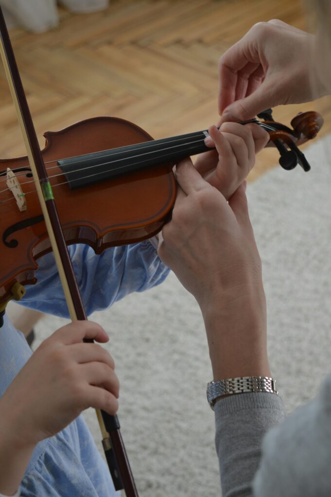 A child receives violin lessons from a teacher, focusing on hand positioning.